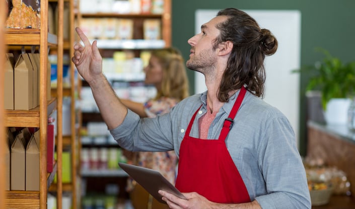 Male staff holding a digital tablet and checking grocery products on the shelf in supermarket